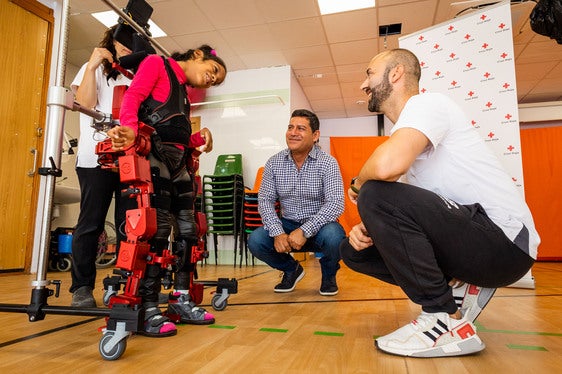 Isabella, junto a su padre y dos monitores de Cruz Roja, camina con el exoesqueleto en el colegio de la entidad en Valencia.