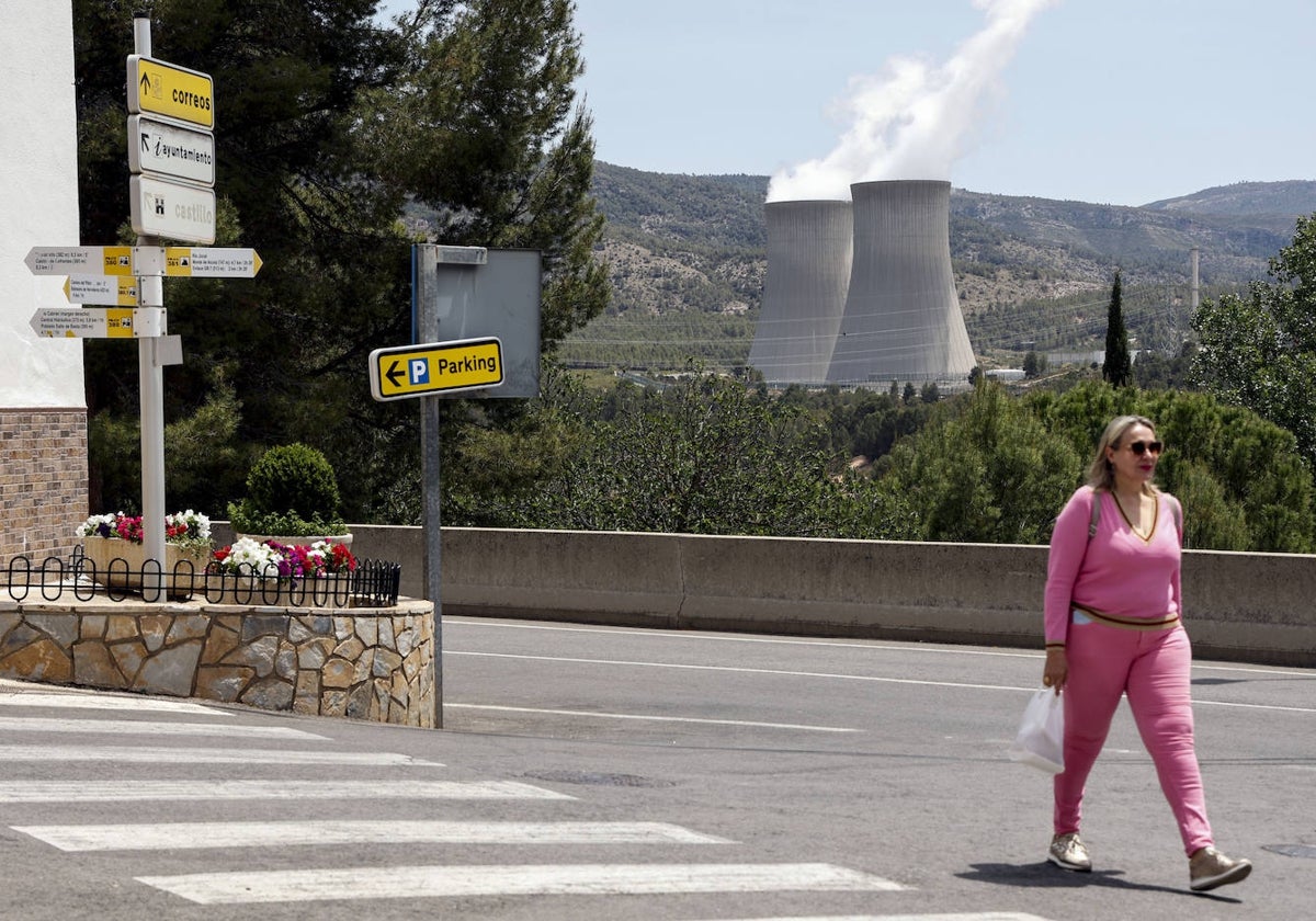 Una vecina cruza una calle de Cofrentes con las torres de la central nuclear al fondo.