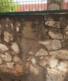 Imagen secundaria 2 - Carteles reivindicativos colocados por la AMPA y desperfectos en la parte exterior del muro perimetral. Se observan zonas donde la piedra se está desgajando, grietas y reparaciones anteriores. 