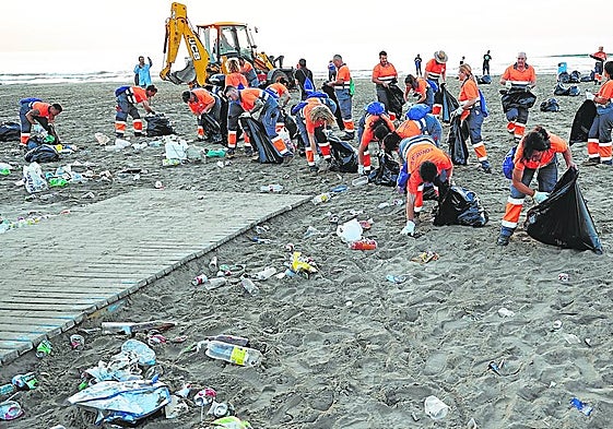 Los trabajadores de limpieza recogen la basura de la playa de la Malvarrosa después de San Juan.