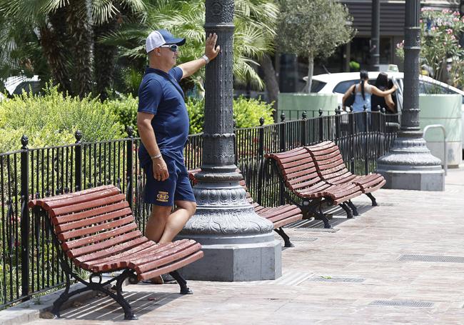 Un hombre se refugia del sol tras una farola en la plaza del Ayuntamiento de Valencia.