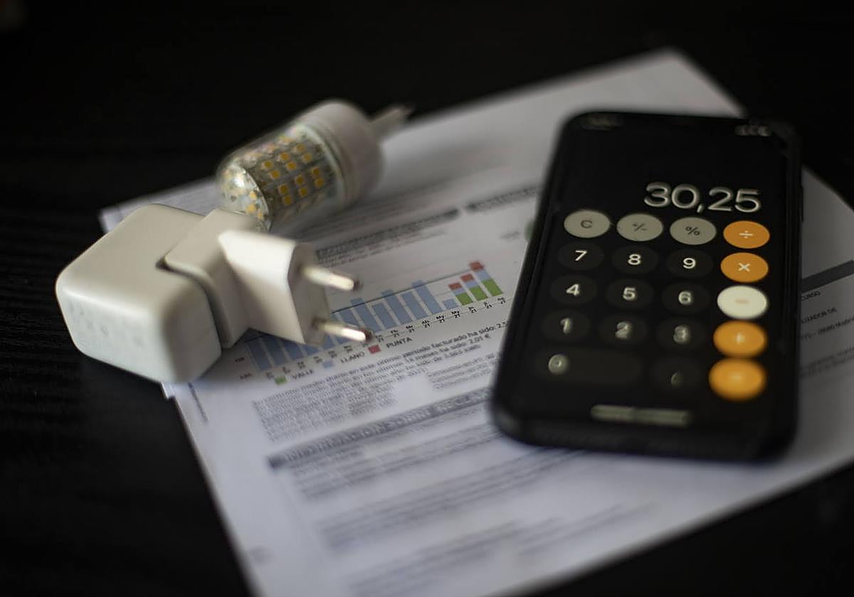 Una factura de la luz junto a un móvil y un enchufe