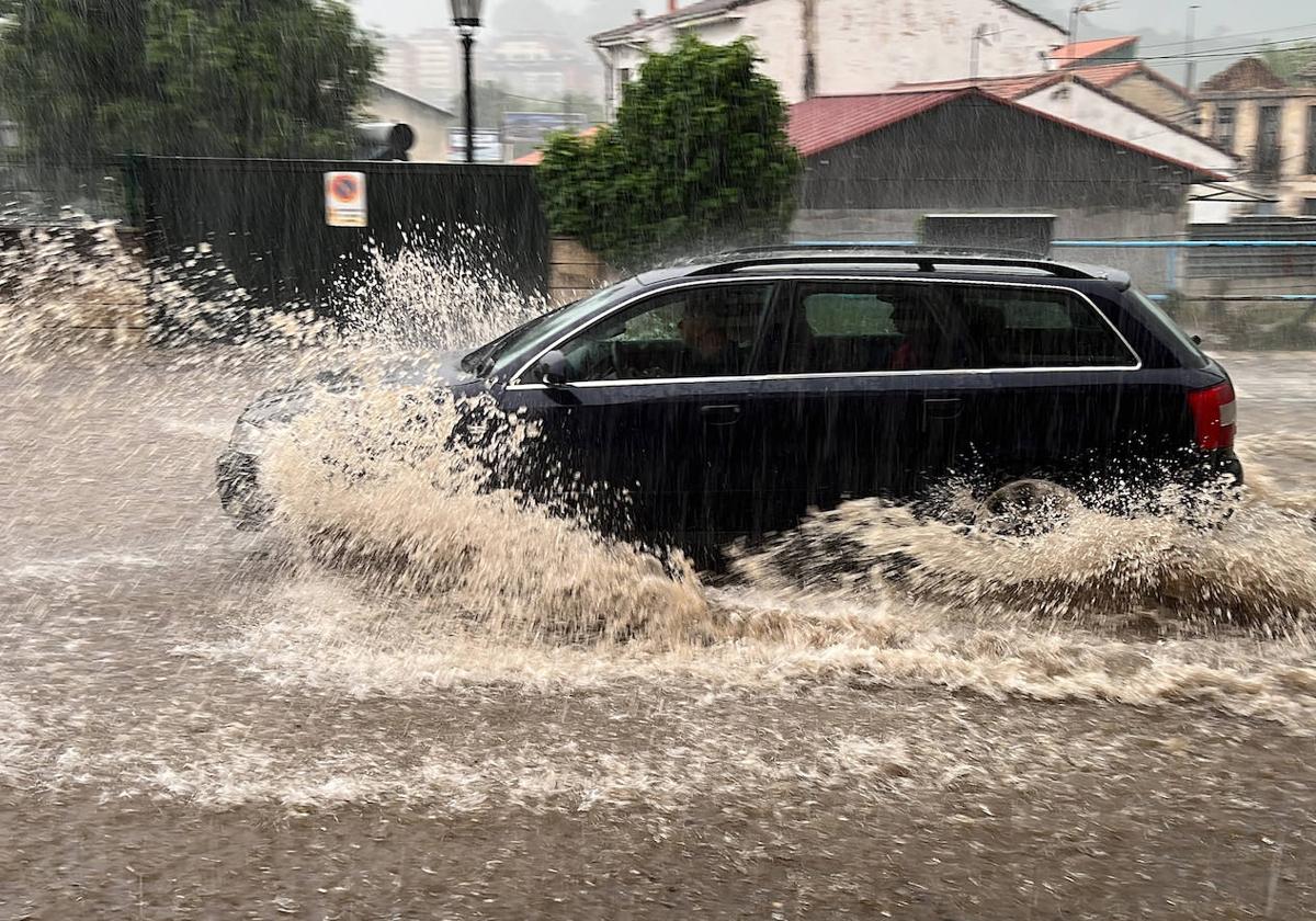 Un coche circula por una carretera inundada.