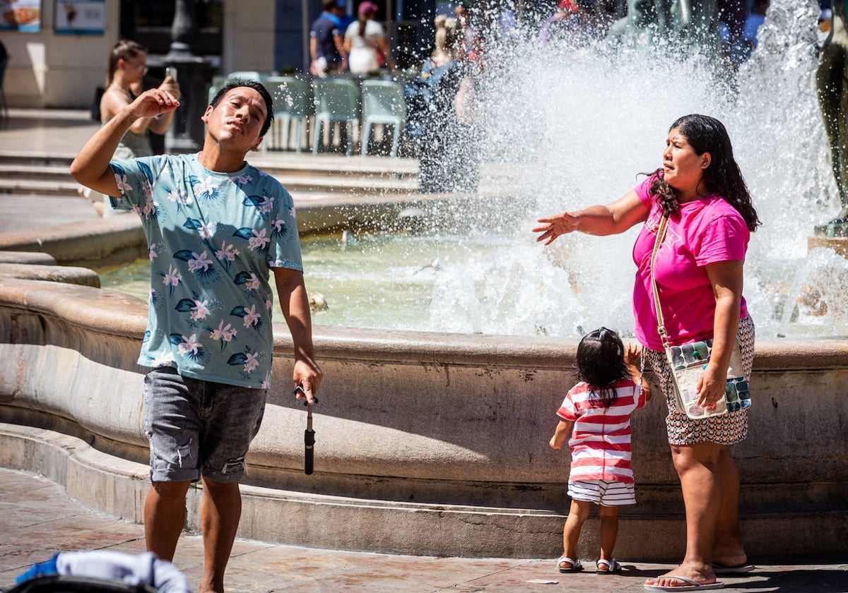 Dos personas se intentan refrescar en una fuente.