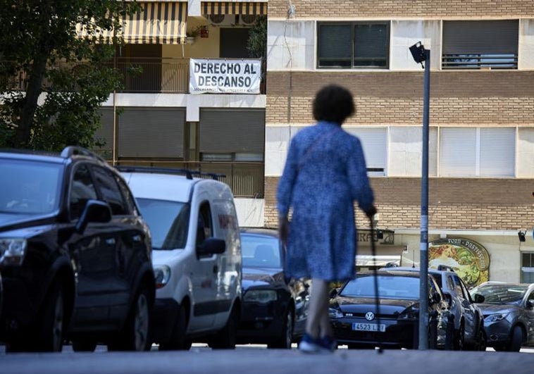 Una mujer recorre el barrio frente a una pancarta que reivindica el derecho al descanso.