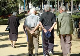 Unos jubilados conversan mientras pasean por un parque.