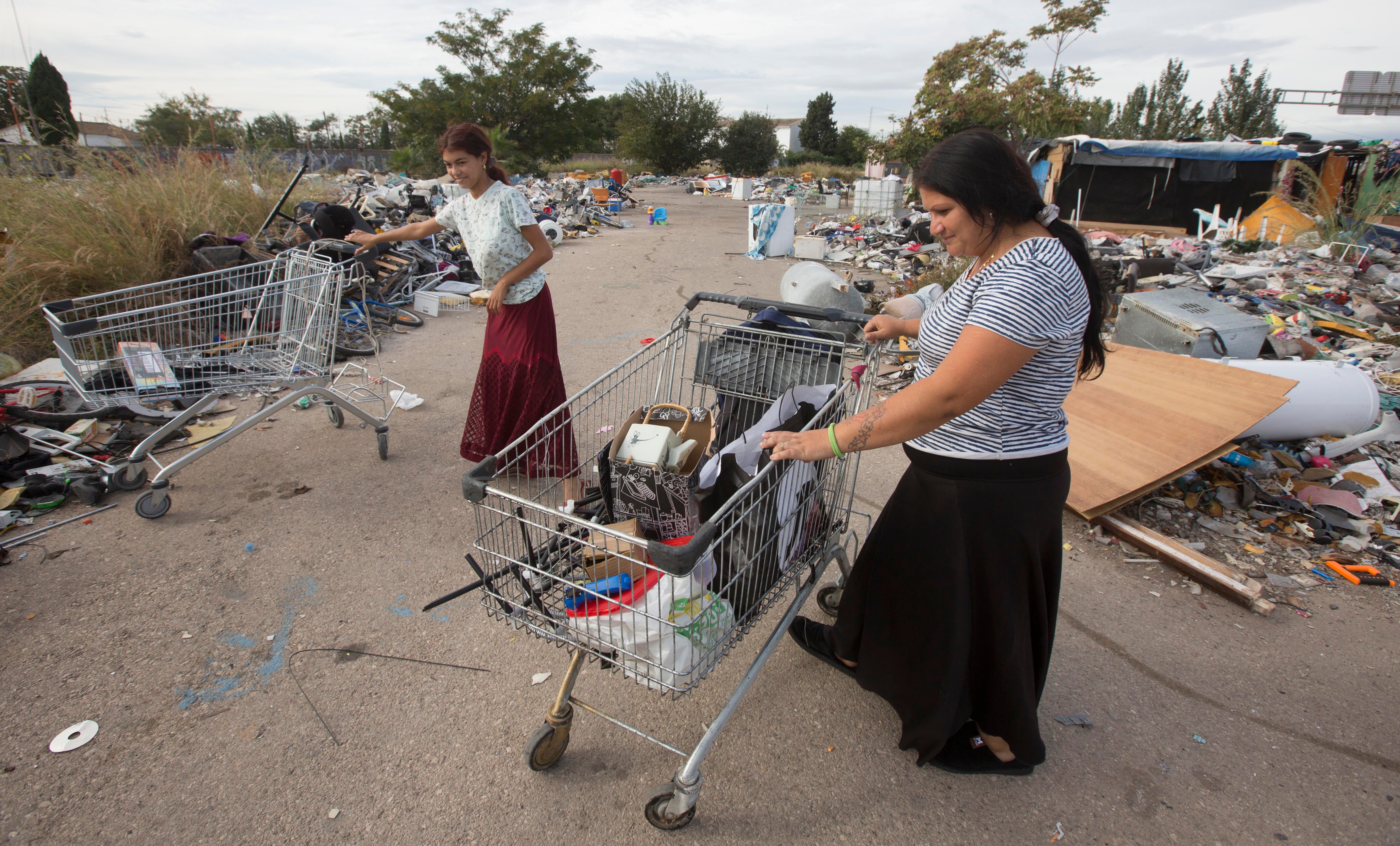 Denisa y Mura, madre e hija, entre montañas de chatarra, con los carros que usan para ganarse el pan y sus casas detrás, en una planta ilegal junto al polígono Vara de Quart.