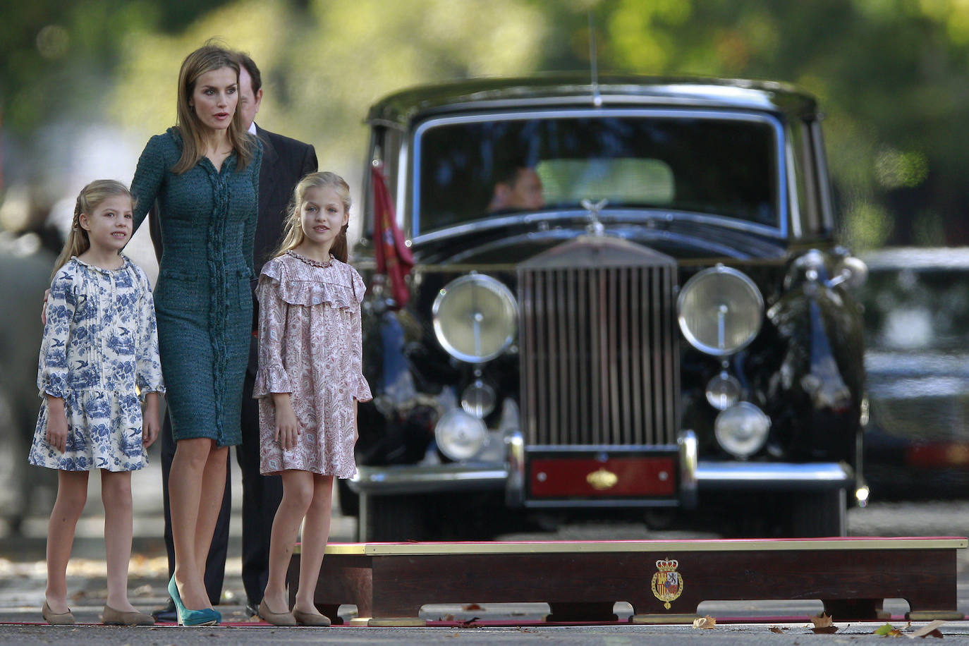 La princesa Leonor, junto a su hermana la infanta Sofía (i) y su madre la reina Letizia, el 12 de octubre de 2014, a la llegada al primer desfile de la Fiesta Nacional en el que se situó a la derecha de Felipe VI para hacer visible su condición de heredera, después de que en años anteriores se hubiera sentado a la izquierda con su madre y su hermana. 