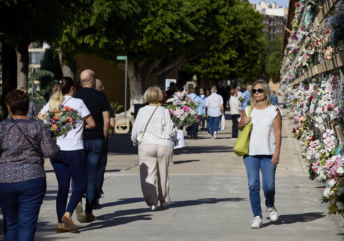 Varias personas en manga corta llevando flores al cementario de Valencia.