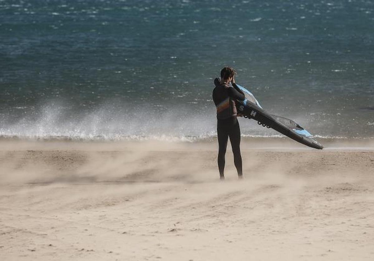 Un joven con la tabla de surf en la playa de la Malvarrosa.