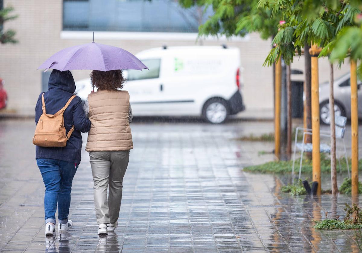 Dos mujeres se protegen del aire y de la lluvia en Valencia bajo un paraguas.