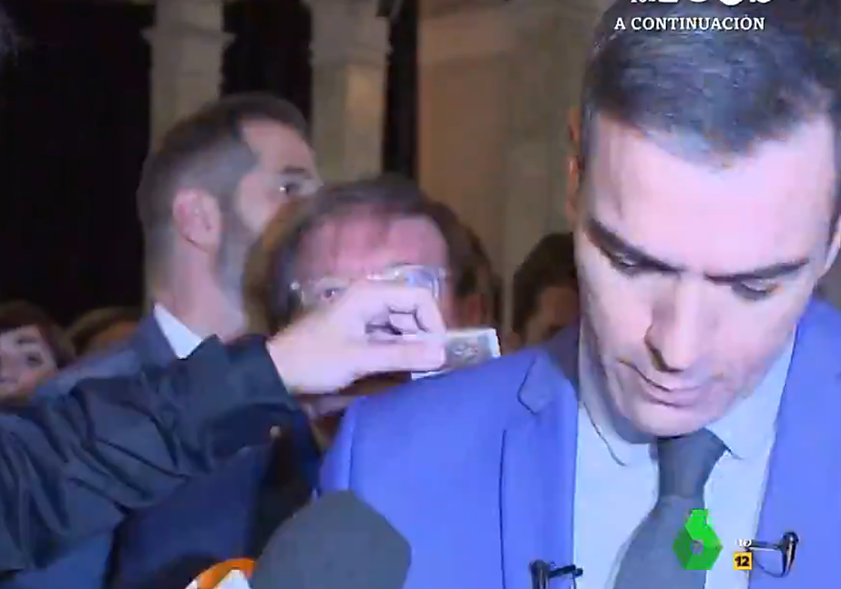 Imagen del momento en el que el reportero le pasa el décimo por la espalda a Pedro Sánchez.