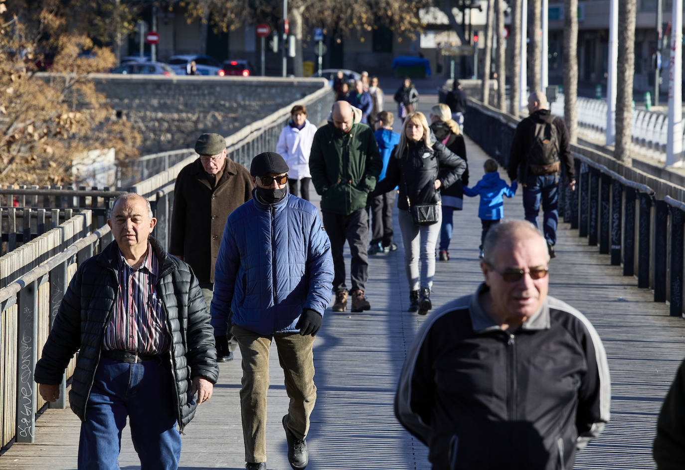 Varias personas caminan abrigadas por una pasarela del río de Valencia.