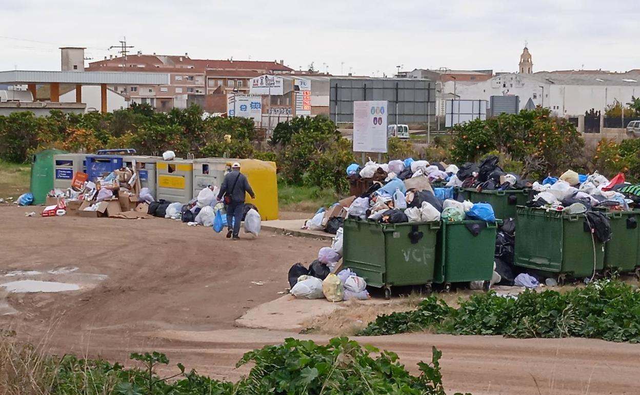 Un hombre deposita bolsas de basura junto a contenedores a rebosar. 