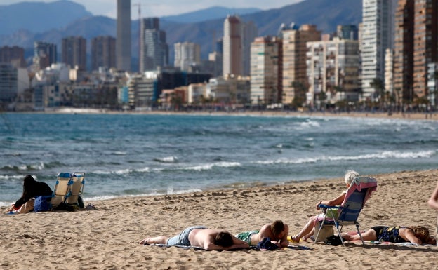 Varias personas toman el sol en la playa de Benidorm, donde el termómetro ha rozado los 20 grados en las horas centrales del día. 