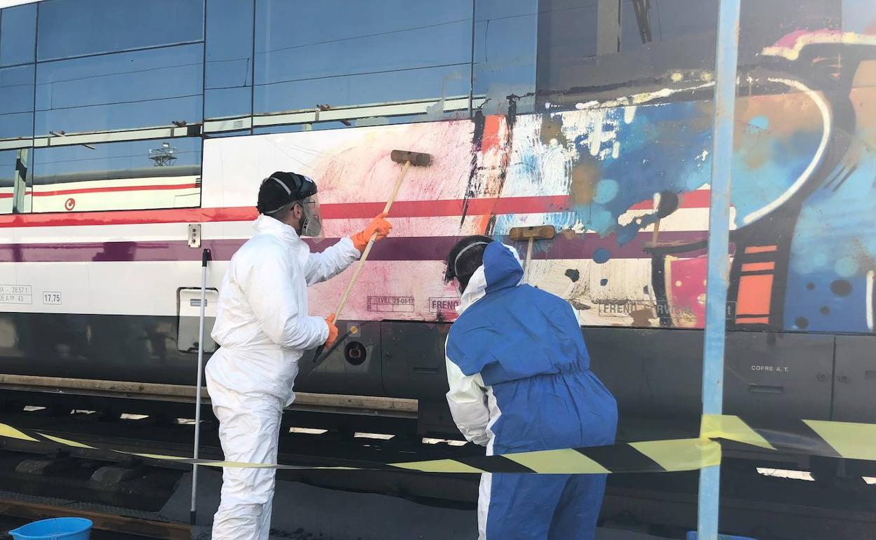 Operarios limpian grafitis en un tren. 