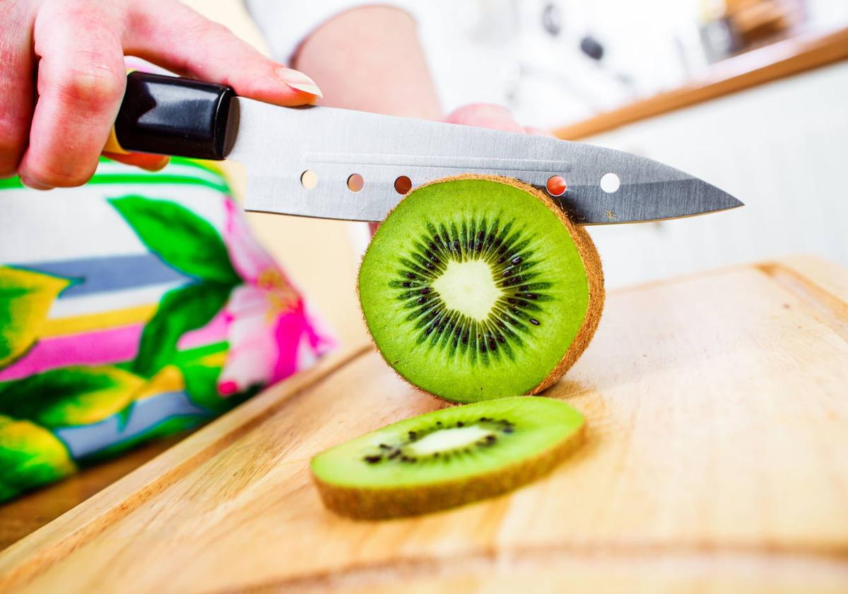 Una mujer corta un kiwi en rodajas.