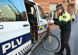 Un agente de la Policía Local de Valencia retira una bicicleta abandonada en la vía pública, después de cumplirse los 30 días de aviso.