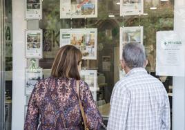 Una pareja mira anuncios de pisos en una inmobiliaria.