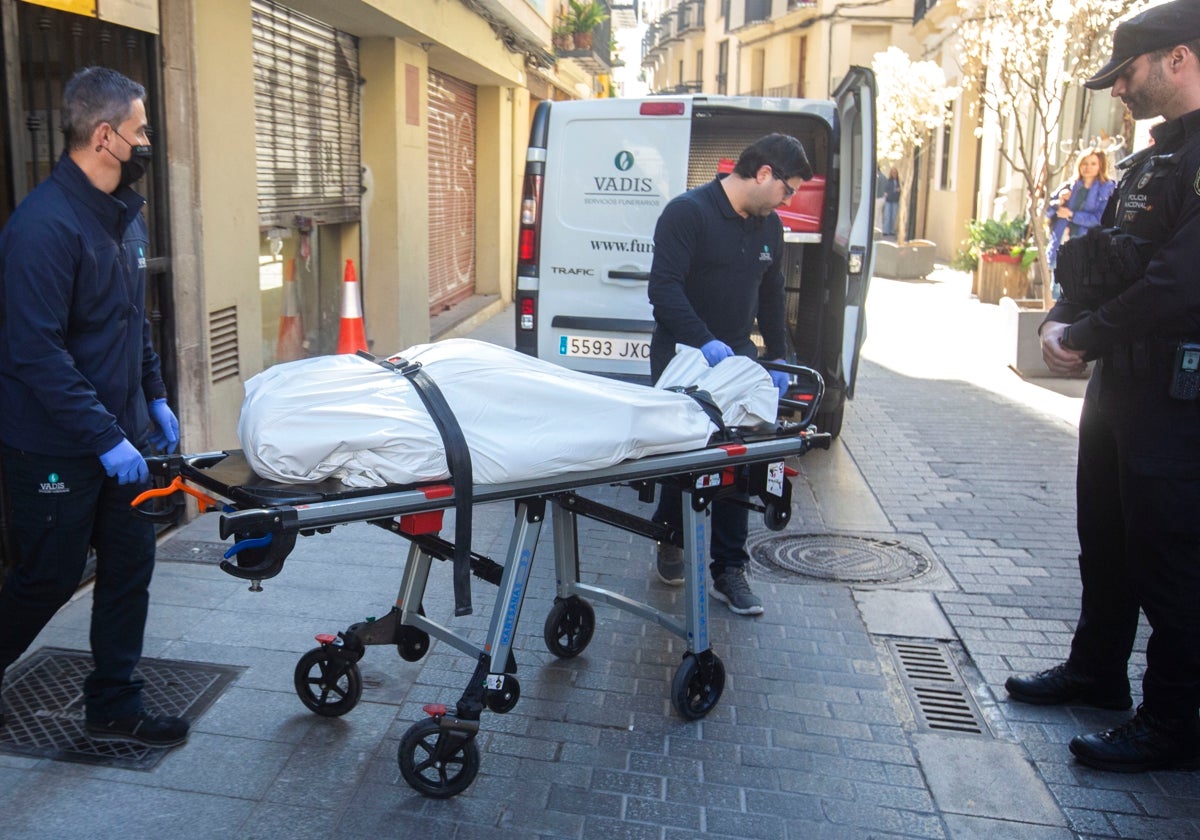 Dos empleados del retén fúnebre sacan el cadáver del edificio.