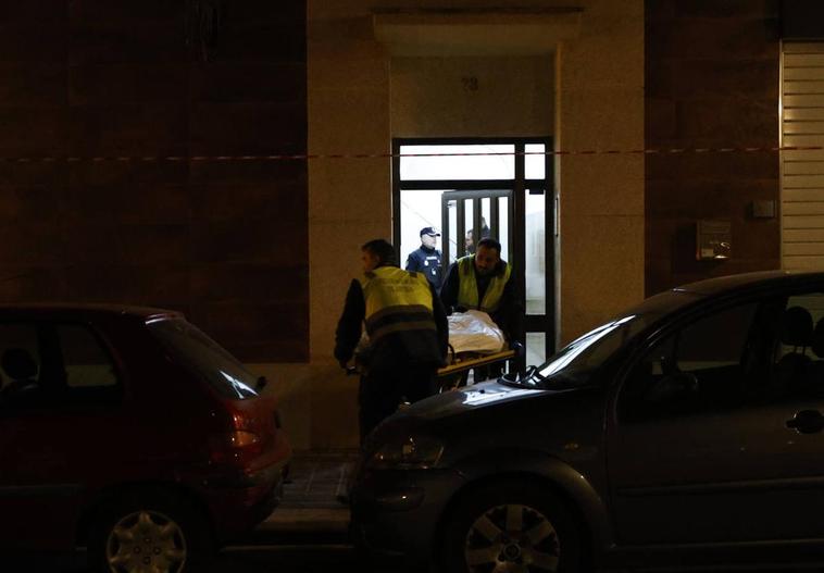 Dos trabajadores del retén fúnebre trasladan el cadáver de la mujer.