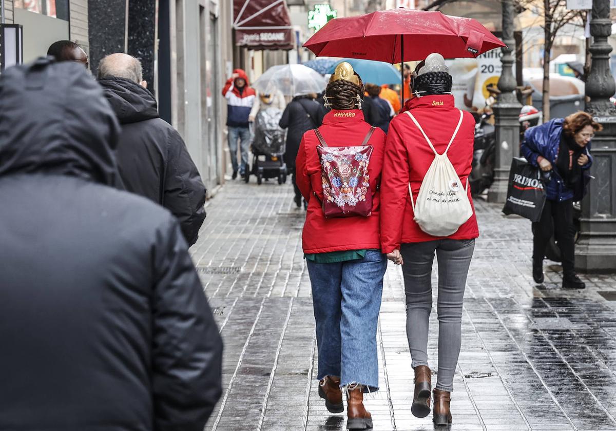 Dos falleras se refugian de la lluvia en una imagen de archivo.