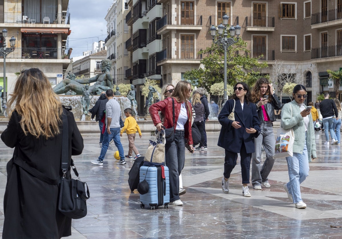 Varias viajeras pasean por la plaza de la Virgen con sus maletas tras llegar a Valencia.