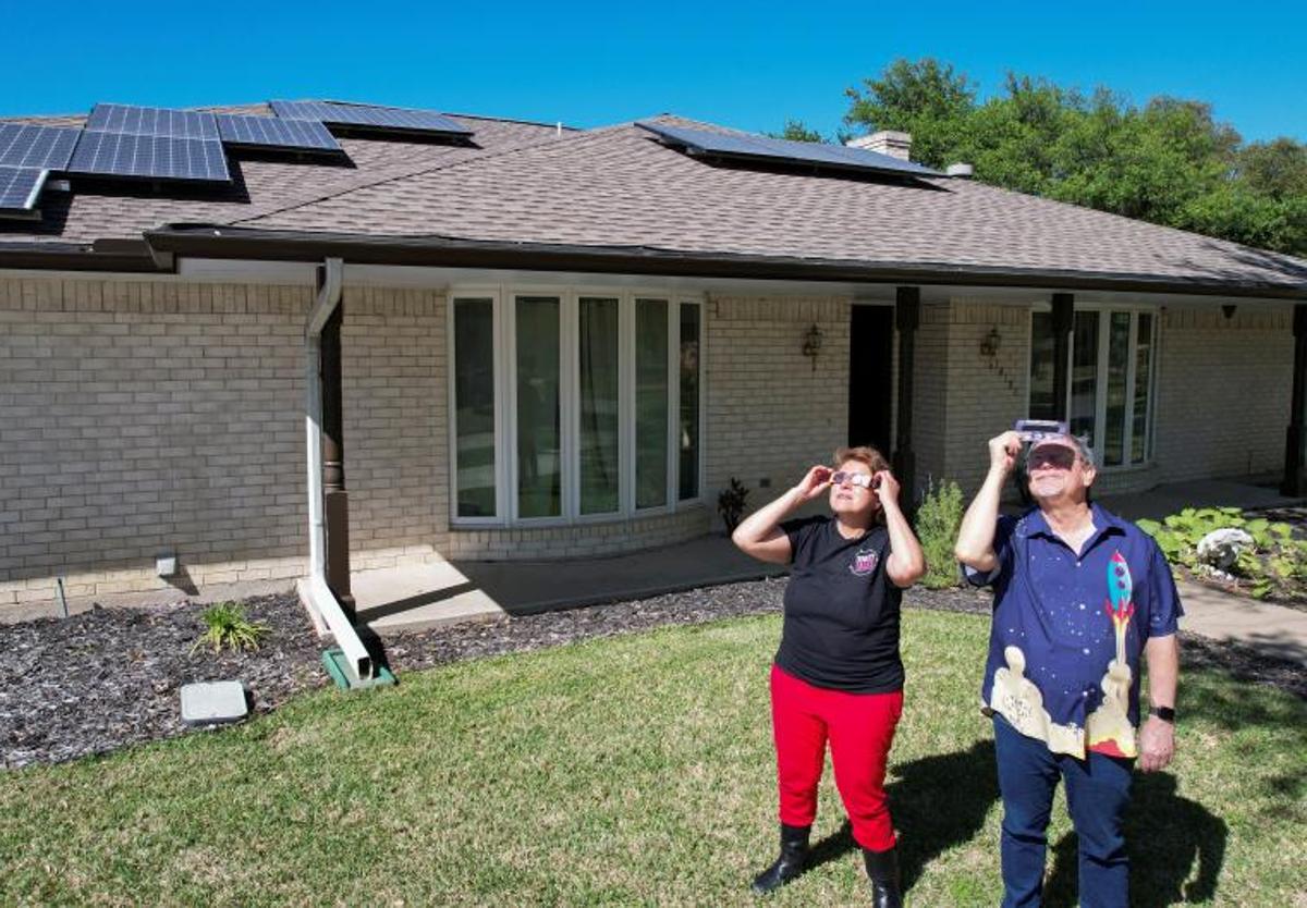 La cazadora de eclipses Leticia Ferrer y su esposo Daniel Brookshier observan el sol a través de gafas de eclipse, frente a su casa en Dallas.