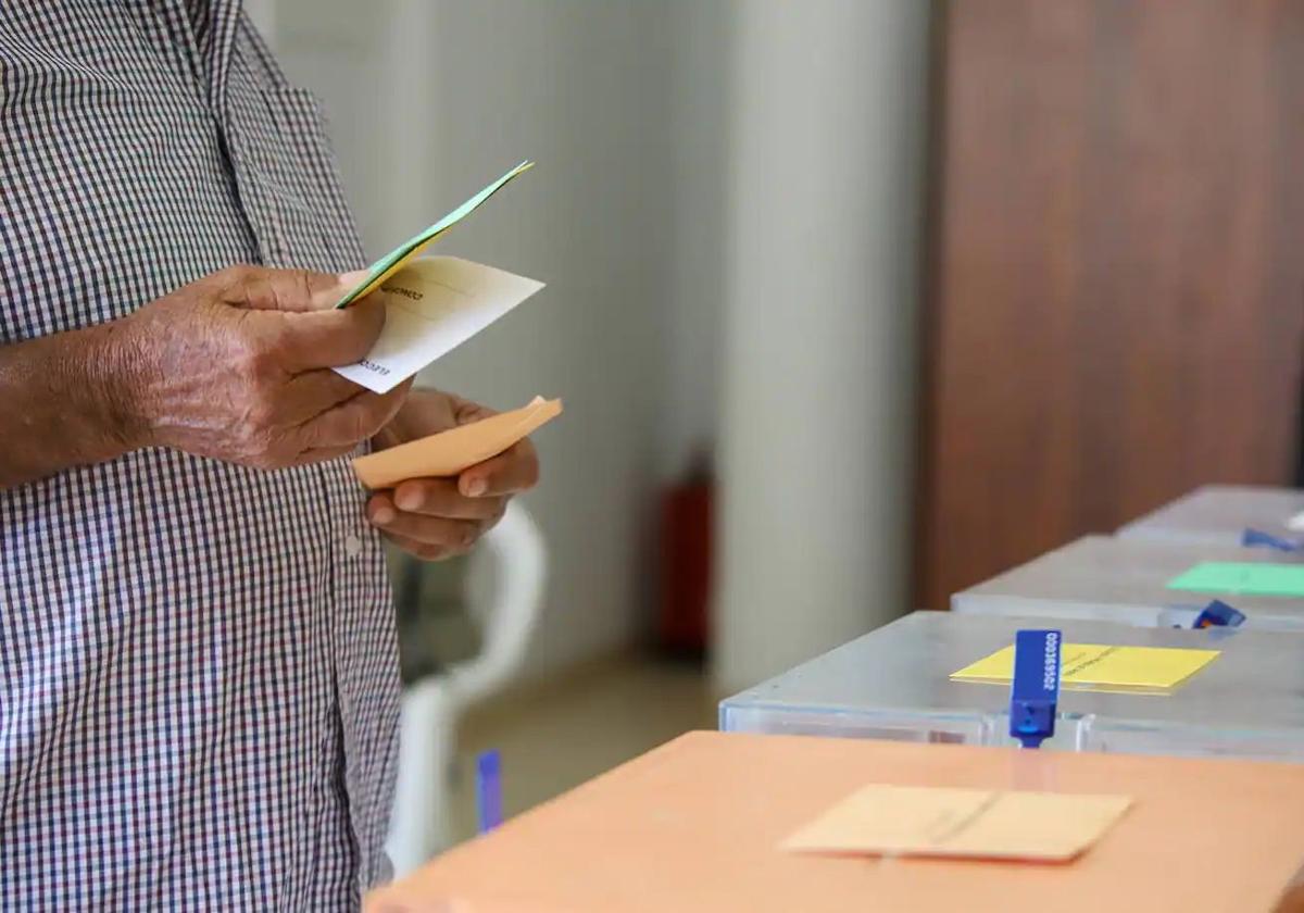 Un hombre sostiene sus papeletas de votación ante las urnas de la mesa en el colegio electoral