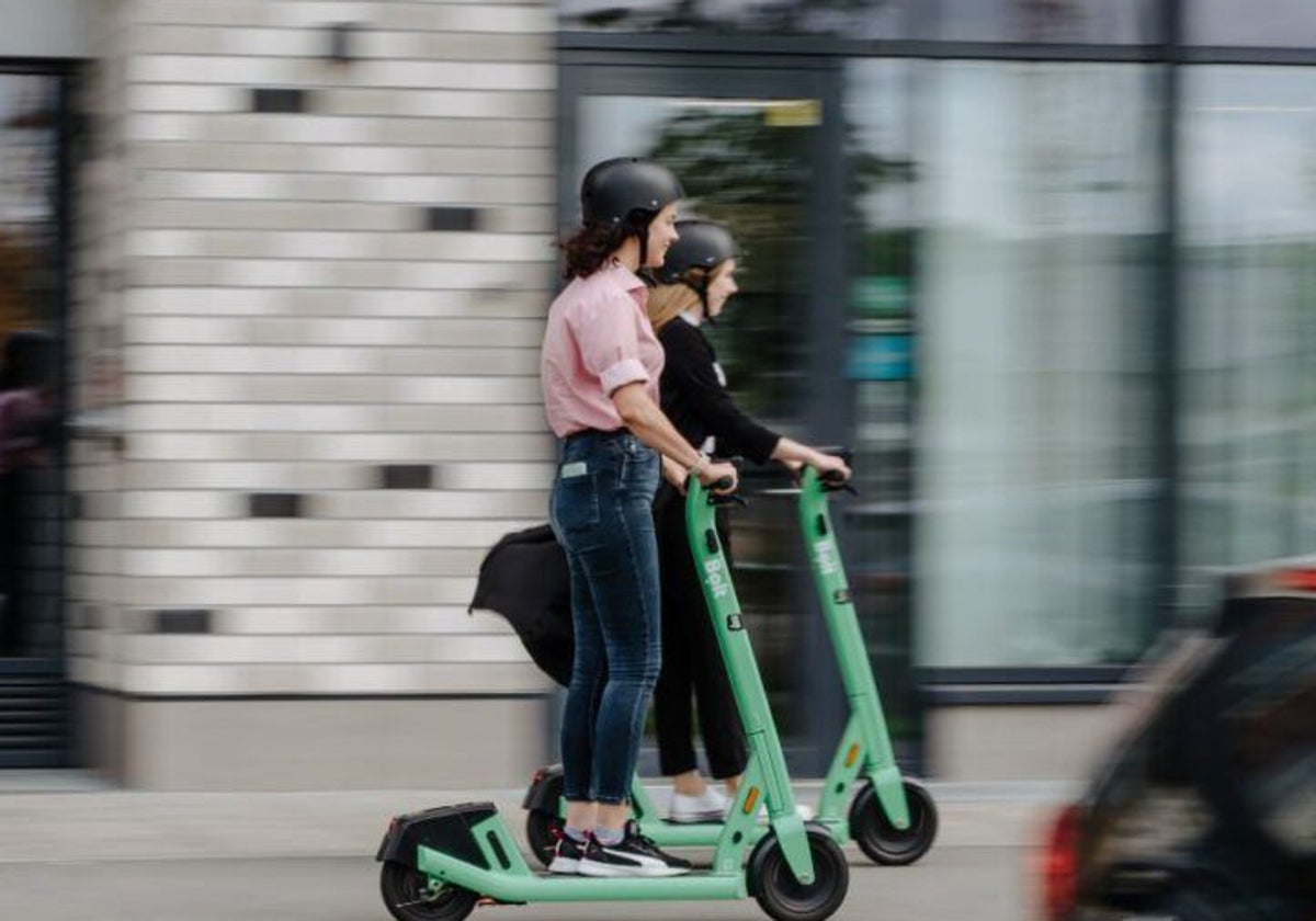 Dos usuarias de patinetes eléctricos, con casco.