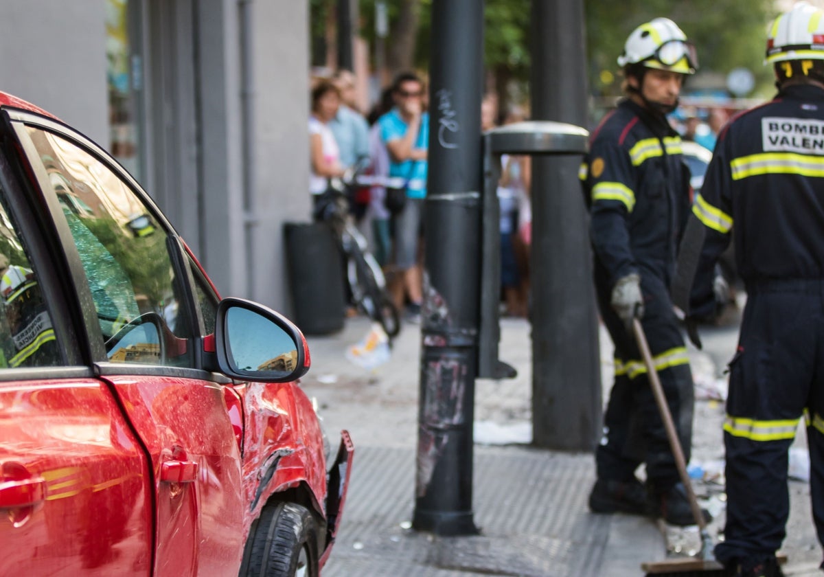 Dos bomberos junto a un vehículo siniestrado en Valencia, en una imagen de archivo.