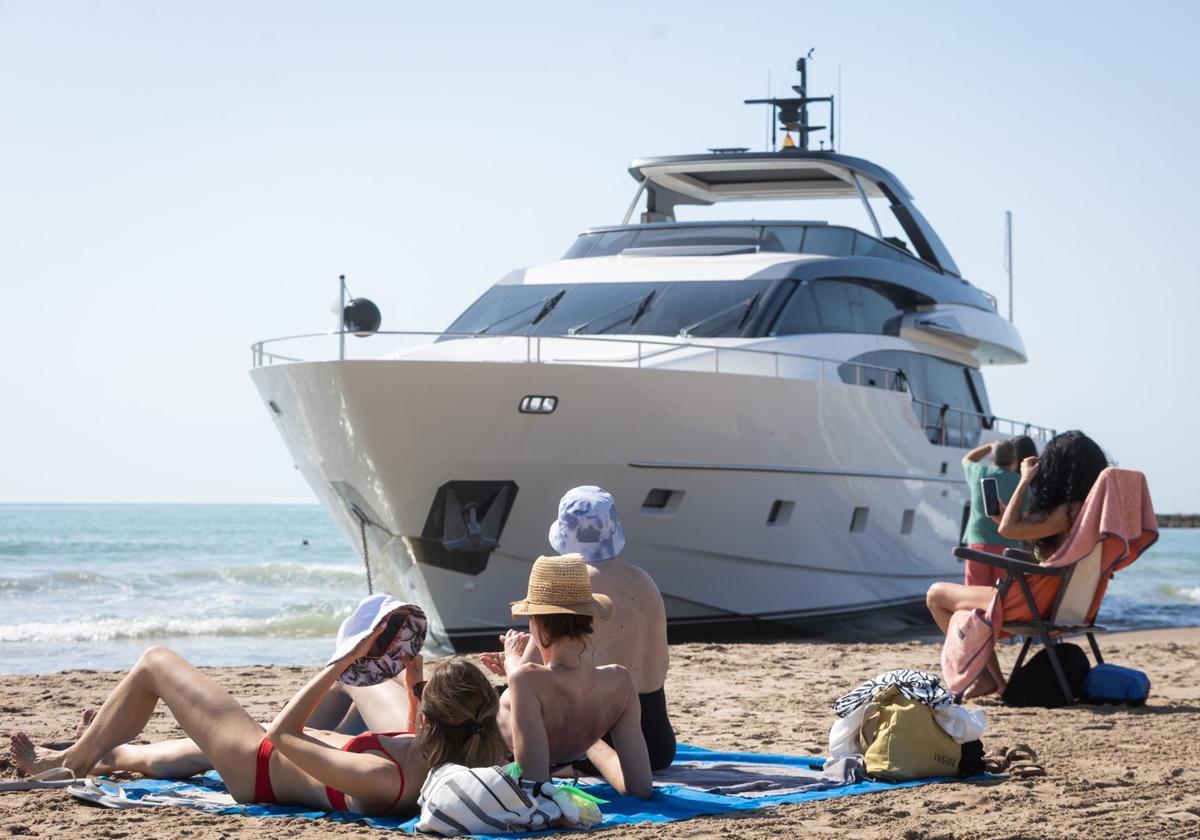 Bañistas, este miércoles, junto al yate encallado en la playa de Pinedo.