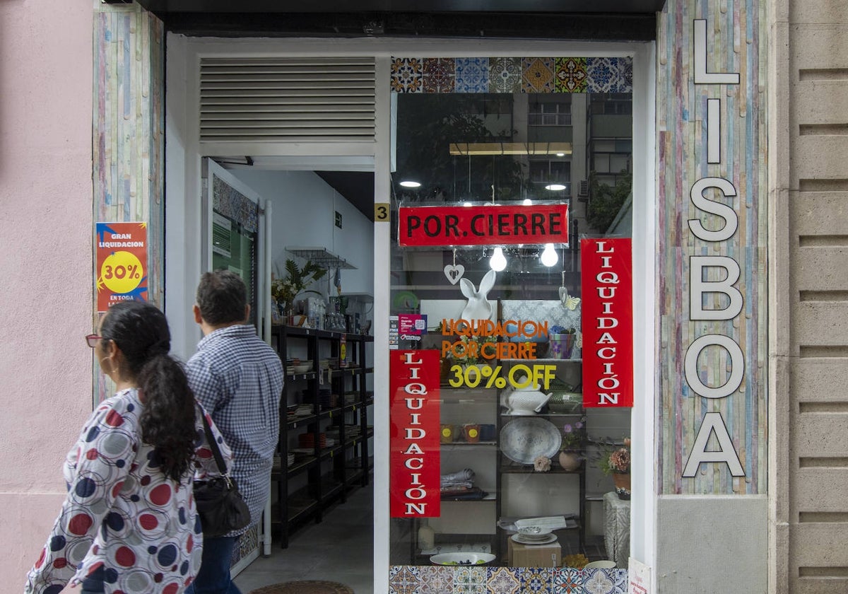 Dos peatones, frente a un negocio en liquidación en la calle Pintor Benedito de Valencia.