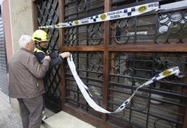 Un bombero quita el precinto del edificio antes de acompañar a un vecino para que recoja sus enseres.