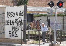 Un vecino cruza el paso a nivel de Alfafar junto a una pintada que alerta de su peligrosidad, esta semana.