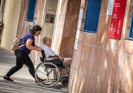 Una mujer lleva a hombre en silla de ruedas al centro de salud.