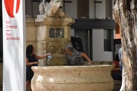 Varias personas bebiendo agua en una fuente de Xàtiva.