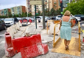 Una mujer atraviesa una pasarela peatonal para sortear un tramo de las obras que hoy siguen activas en la avenida del Cid de Valencia.