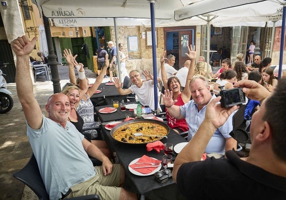 Un grupo de turistas posa para una foto antes de comer una paella en un restaurante.