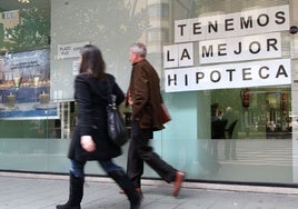 Dos personas pasan ante el escaparate de un banco con publicidad de hipotecas.