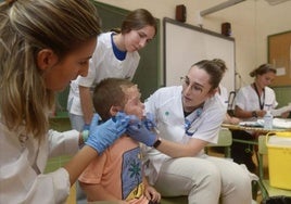 Un equipo sanitario vacuna a un niño en un colegio.