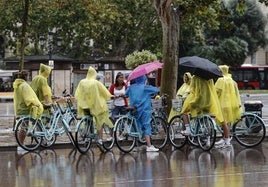 Un grupo de turistas en bicicleta cubiertos con chubasqueros en la plaza del Ayuntamiento.