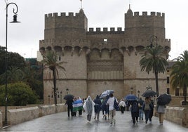 Viandantes que se protegen de la lluvia junto a las torres de Serranos.