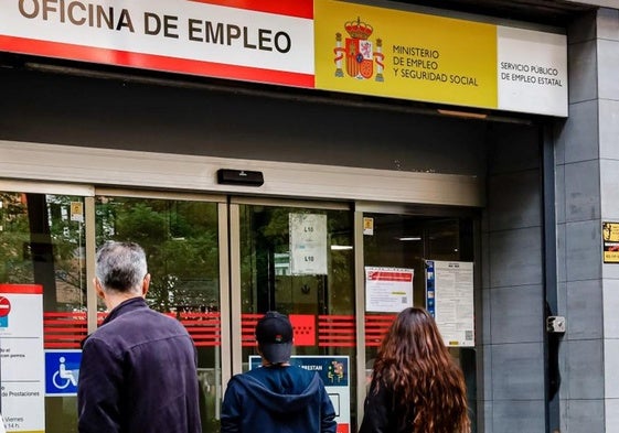 Tres personas esperan a la puerta de una oficina de empleo.