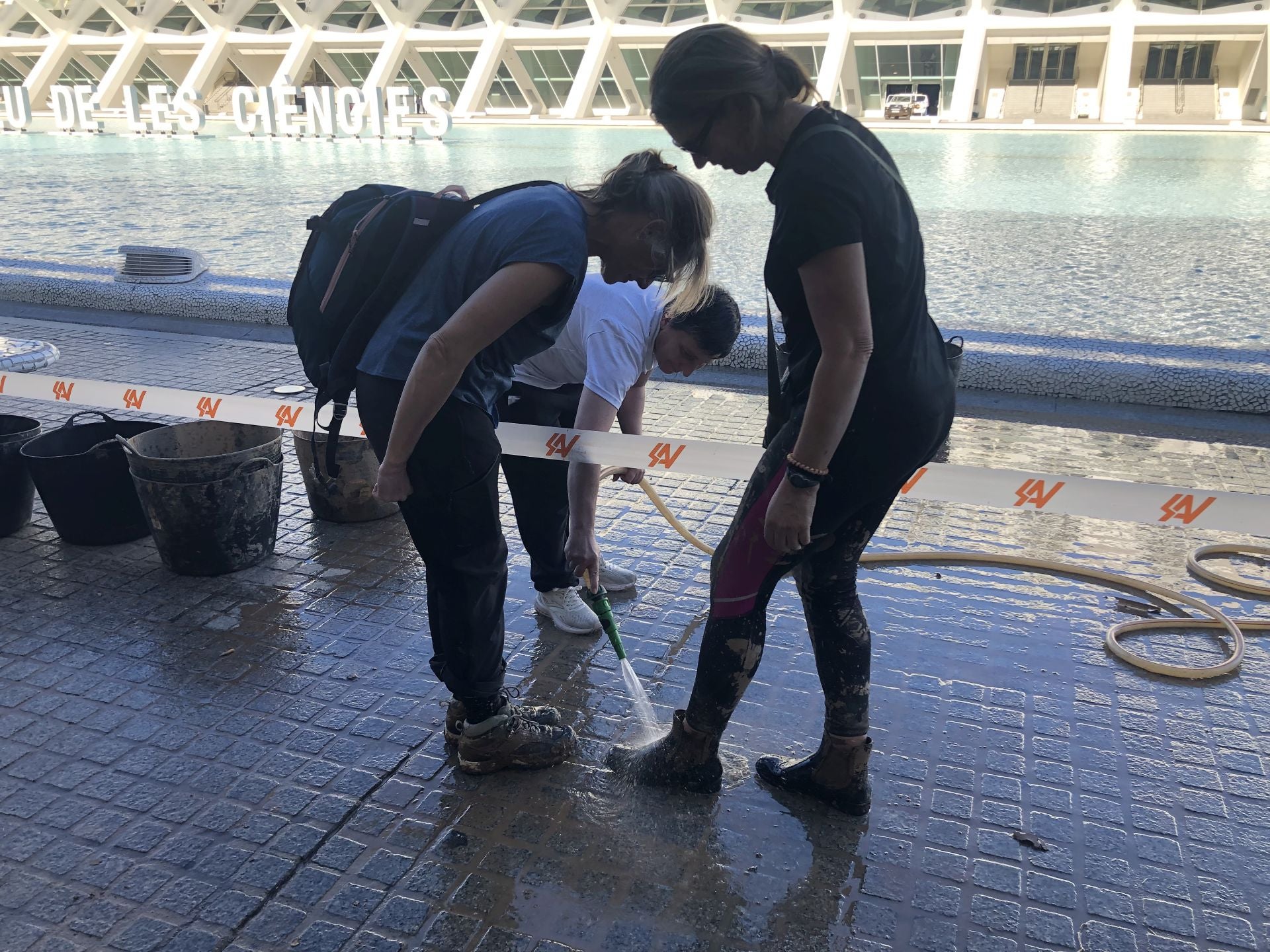 Amparo limpia a manguerazos las botas de Ana y Olga.