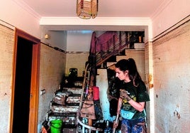 Una mujer quita el barro en una vivienda en la que la lámpara recoge la huella del agua.