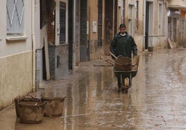 Un vecino traslada en carretilla restos de utensilios para limpiar el barro, bajo la lluvia de este miércoles en Paiporta.