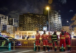 Bomberos de la UME observan el edificio destruido por el fuego junto al vallado del perímetro de seguridad.