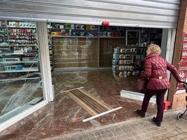 Una vecina de la calle Sagunto se asoma a la tienda asaltada con los cristales destrozados.