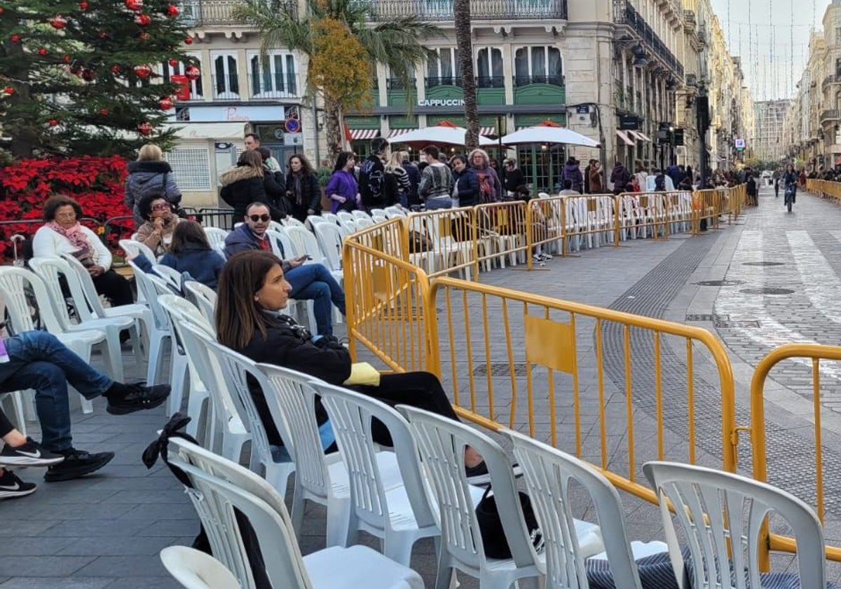 Varias personas sentadas en las sillas en la plaza de la Reina de Valencia.